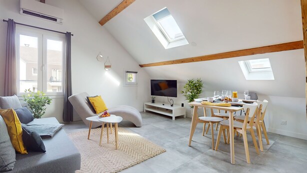 A modern loft apartment with a dining area, a sofa, a TV, and a balcony with skylights.