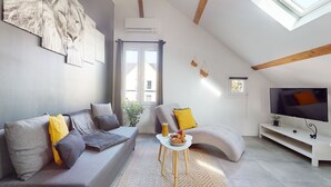 A modern living room with a grey sofa, a smaller armchair, a coffee table, and a TV on a white stand.