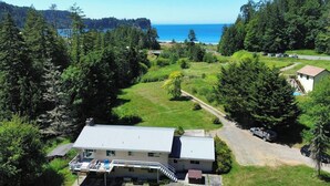 A house with a large deck, surrounded by dense forest and a view of the ocean. - Crescent Beach Retreat: Cozy 4br House (Port Angeles)