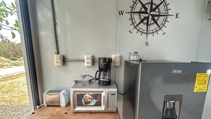 Een compacte kitchenette met een magnetron, broodrooster en koffiezetapparaat op een klein tafeltje, een koelkast, en een kompas als wanddecoratie.