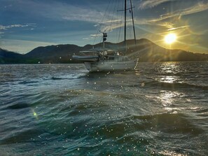 Una barca a vela su acque calme con un tramonto sullo sfondo.