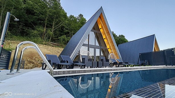 Un edificio moderno con un diseño triangular único, una piscina y asientos exteriores junto a la piscina.