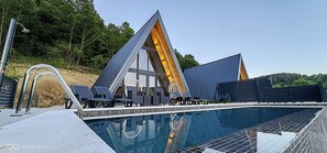 Een modern gebouw met een opvallend dak in driehoeksvorm, een zwembad en een terras aan het zwembad.