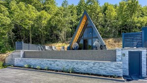 Una estructura de vidrio moderna y triangular con techo plano, rodeada por un muro de piedra y una cerca de metal.