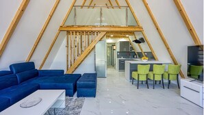 Un loft moderno con techo alto, un comedor con sillas verdes, un sofá azul y una cocina al fondo.