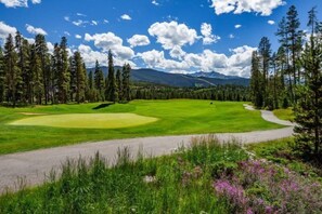 A golf course with a clear path, surrounded by tall pine trees and mountains in the background. - West Keystone Condominiums (Keystone)