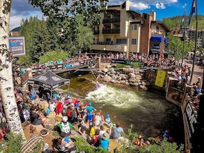 A crowded outdoor event with a river, spectators, and a bridge. - Cascade Village Residences (Vail)