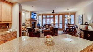 A spacious kitchen with granite countertops, a stone fireplace, and a dining area with wooden furniture. - The Timbers Ski In Ski Out at River Run (Keystone)