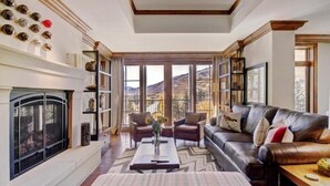 Un salon spacieux doté d’une cheminée, d’un canapé en cuir et de grandes fenêtres offrant une vue sur les montagnes.