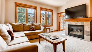 A living room with a sofa, a coffee table, a fireplace, and a TV. - Breckenridge Main Street Condominiums (Breckenridge)