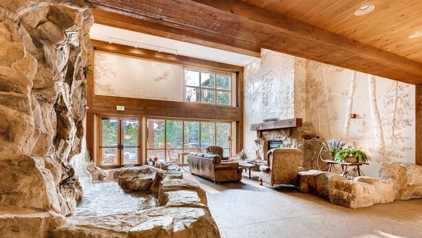 A spacious room with a stone wall, a fireplace, and large windows. - The Springs at River Run (Keystone)