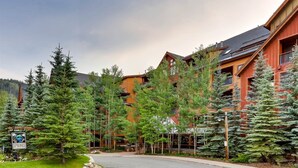 A lodge with multiple wooden buildings, surrounded by evergreen trees, and a paved road leading to the entrance. - The Springs at River Run (Keystone)