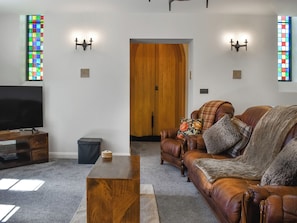 A living room with a television, a wooden coffee table, a brown leather sofa, and two wall-mounted light fixtures.