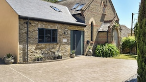 A stone building with a sloped roof, a door, and a small garden area with potted plants.