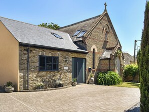 A stone building with a sloped roof, a door, and a small garden area with potted plants.
