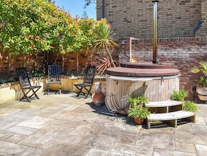 An outdoor patio with a hot tub, seating area, and potted plants.