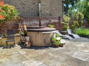 A patio with a hot tub, seating, and potted plants.