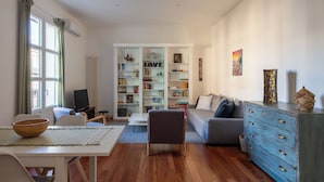 A living room with a white sofa, a blue dresser, a bookshelf, and a dining area with a table and chairs. - Casa Madà vicino al Politeama by Wonderful Italy (Palermo)