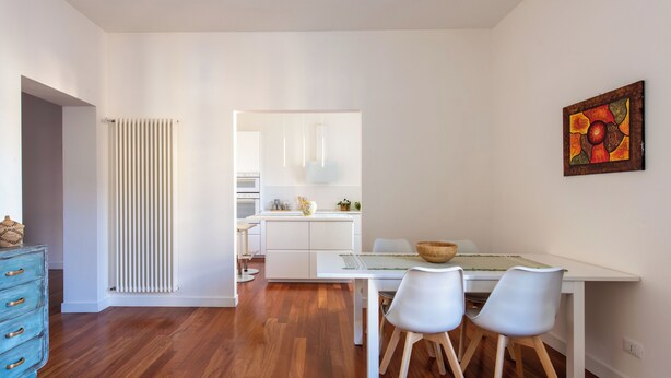 A modern kitchen with white cabinetry, a dining area with a white table and chairs, and a radiator on the wall. - Casa Madà vicino al Politeama by Wonderful Italy (Palermo)