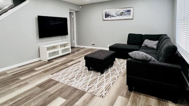 Ein modernes Wohnzimmer mit Flachbildfernseher, schwarzem Sofa und Holzboden.