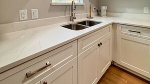A modern kitchen with white cabinetry, a double sink, and a window with blinds. - Stylish Heaven/Central SA (San Antonio)