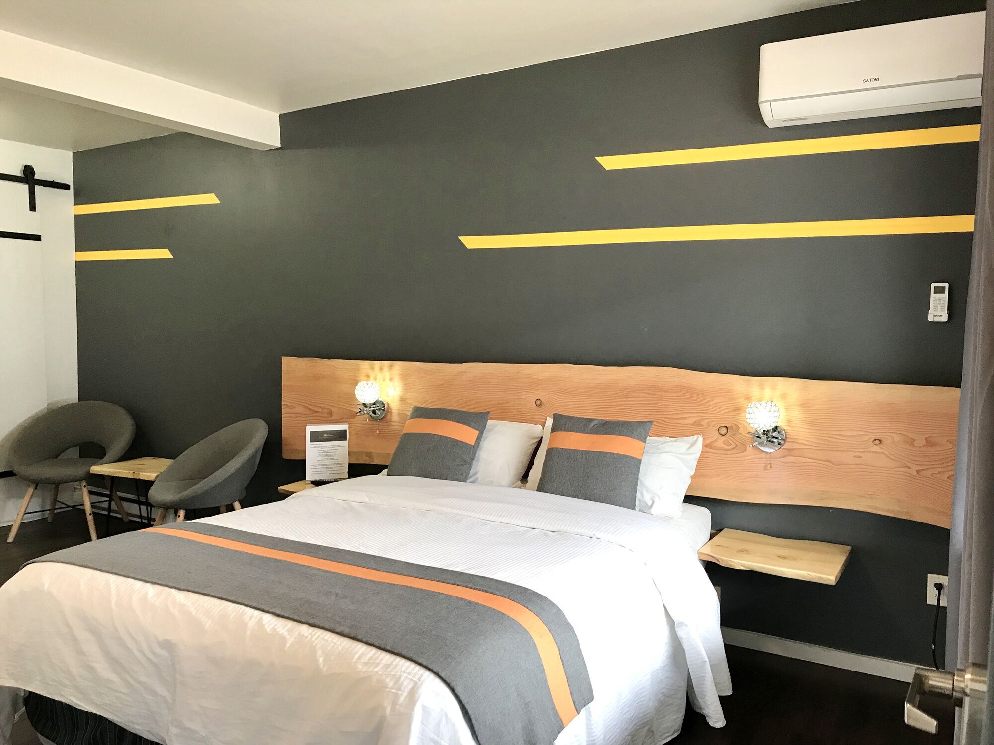 Une chambre d’hôtel moderne dotée d’un grand lit, de deux tables de chevet, d’une tête de lit en bois et d’un climatiseur fixé au mur.