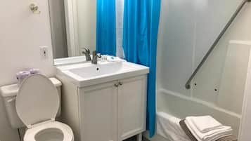 Un baño con inodoro blanco, lavamanos con espejo y zona de ducha con cortina azul.