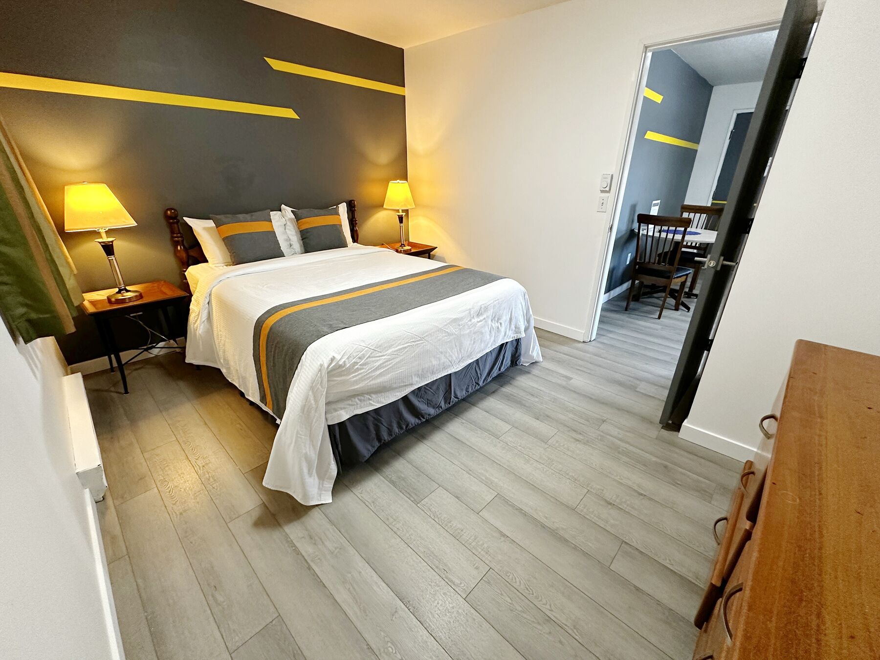 A hotel room with a large bed, two bedside lamps, a wooden headboard, and a grey and white striped bedspread.