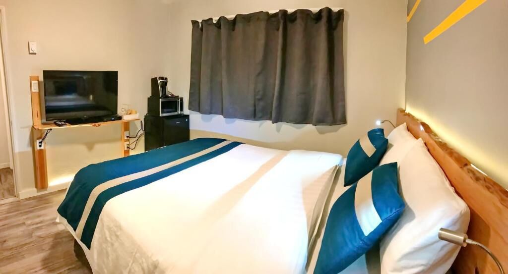 A hotel room with a bed, a TV on a stand, a coffee machine, and a window with curtains.