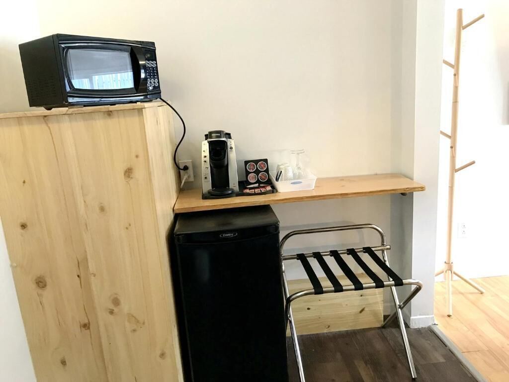 A compact kitchenette with a microwave, coffee maker, and glass containers on a wooden shelf.