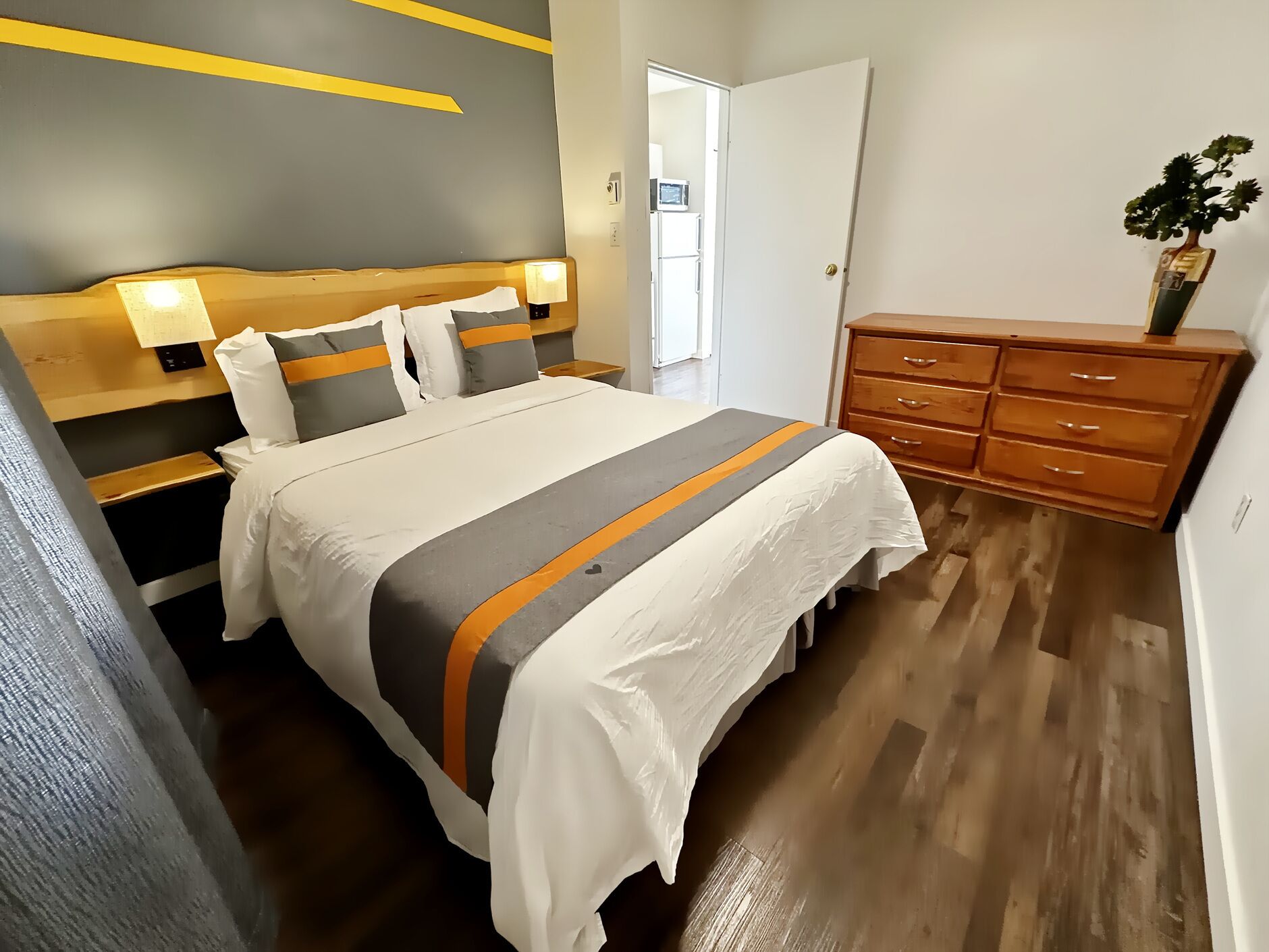 Quarto de hotel com cama, mesas de cabeceira, cômoda e porta.