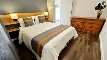 Quarto de hotel com cama, mesas de cabeceira, cômoda e porta.