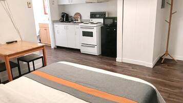 Een slaapkamer met een bed, een houten tafel en een kitchenette met een kookplaat, magnetron en kastjes.