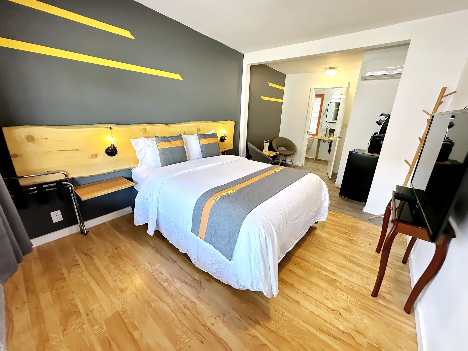 A modern hotel room with a large bed, wooden headboard, and a desk with a chair.