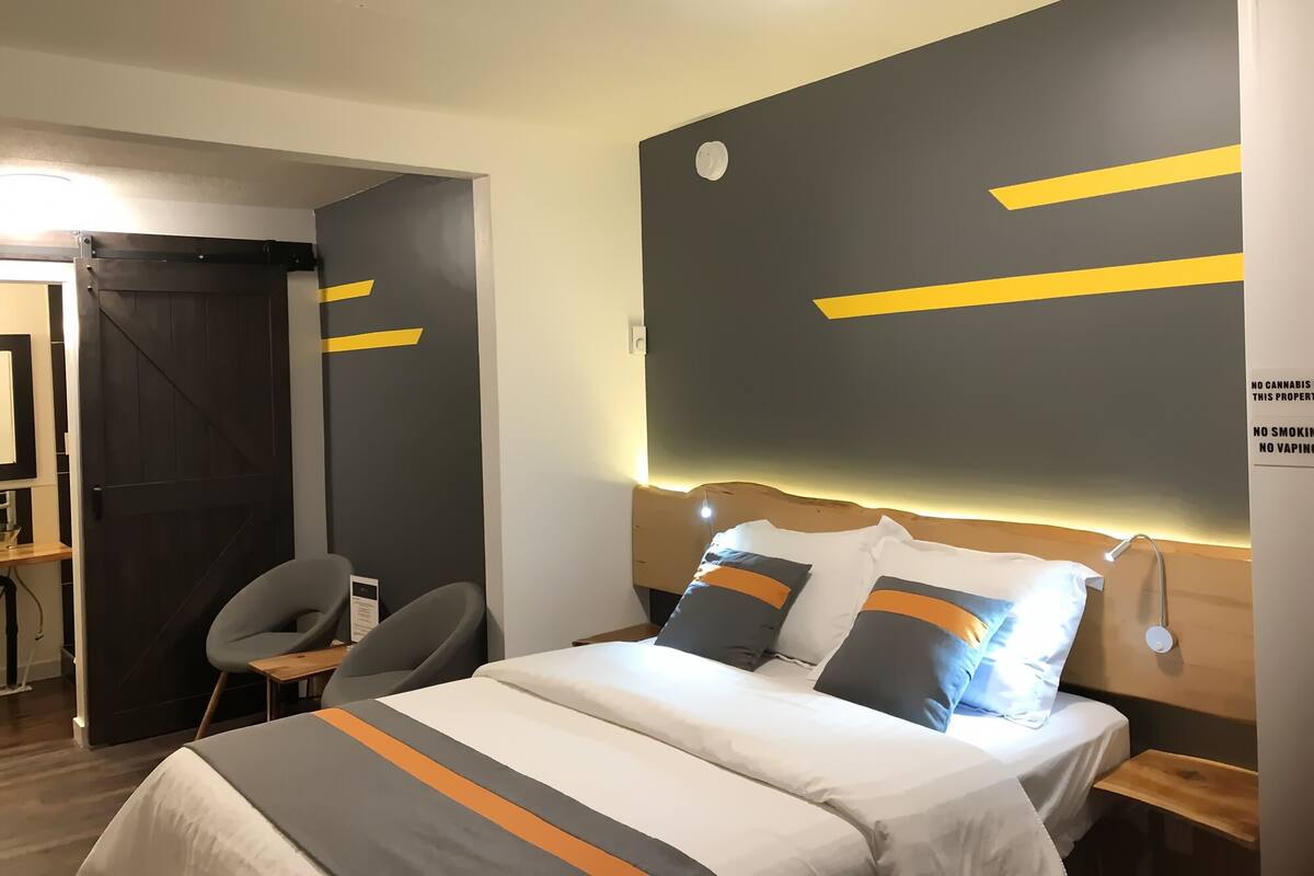 A hotel room with a bed, bedside tables, a desk, and a chair. There is a sign on the wall stating no cannabis, smoking, or vaping.