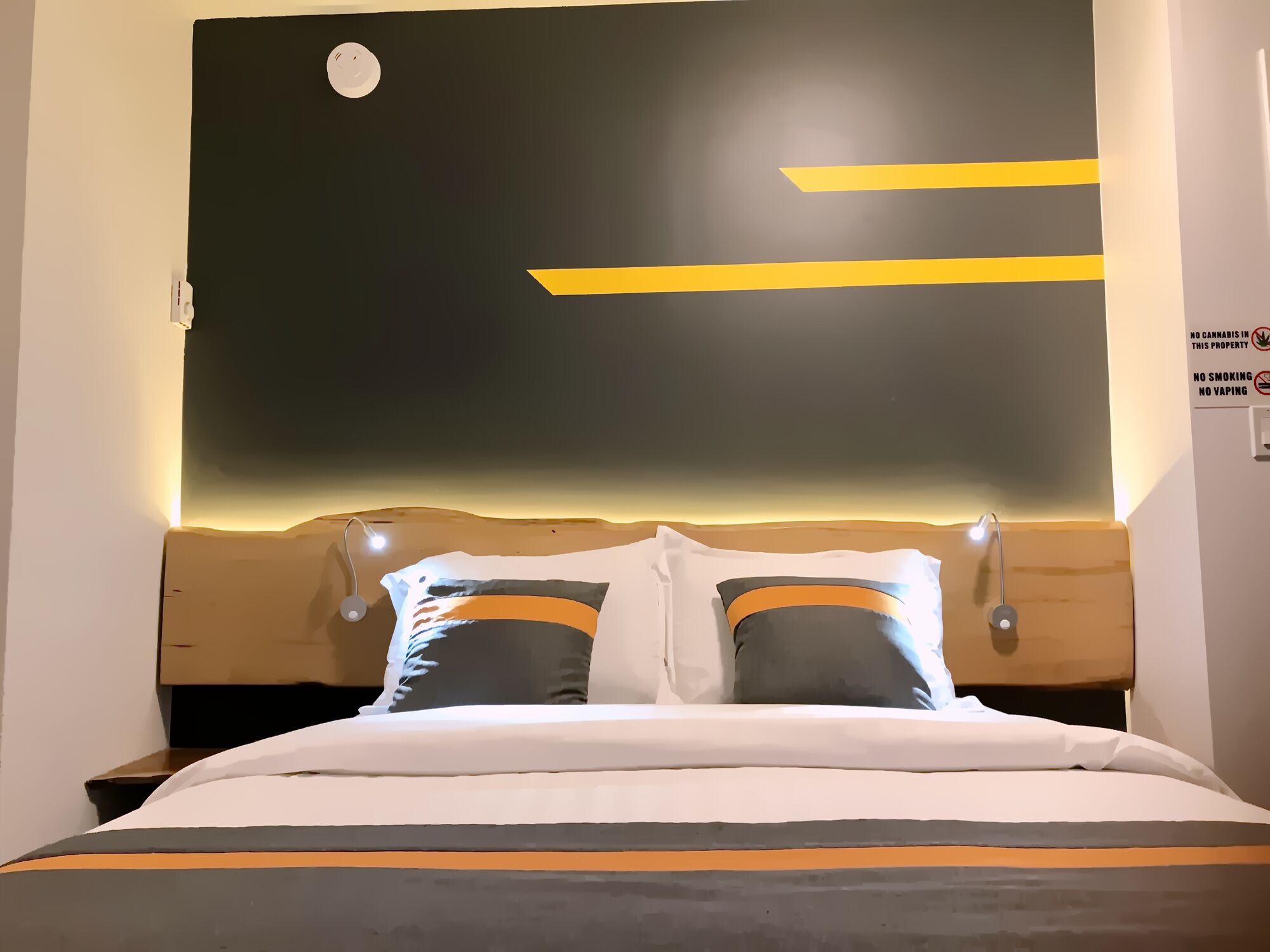 Una habitación de hotel moderna con una cama grande, dos almohadas y un cabecero con una lámpara.