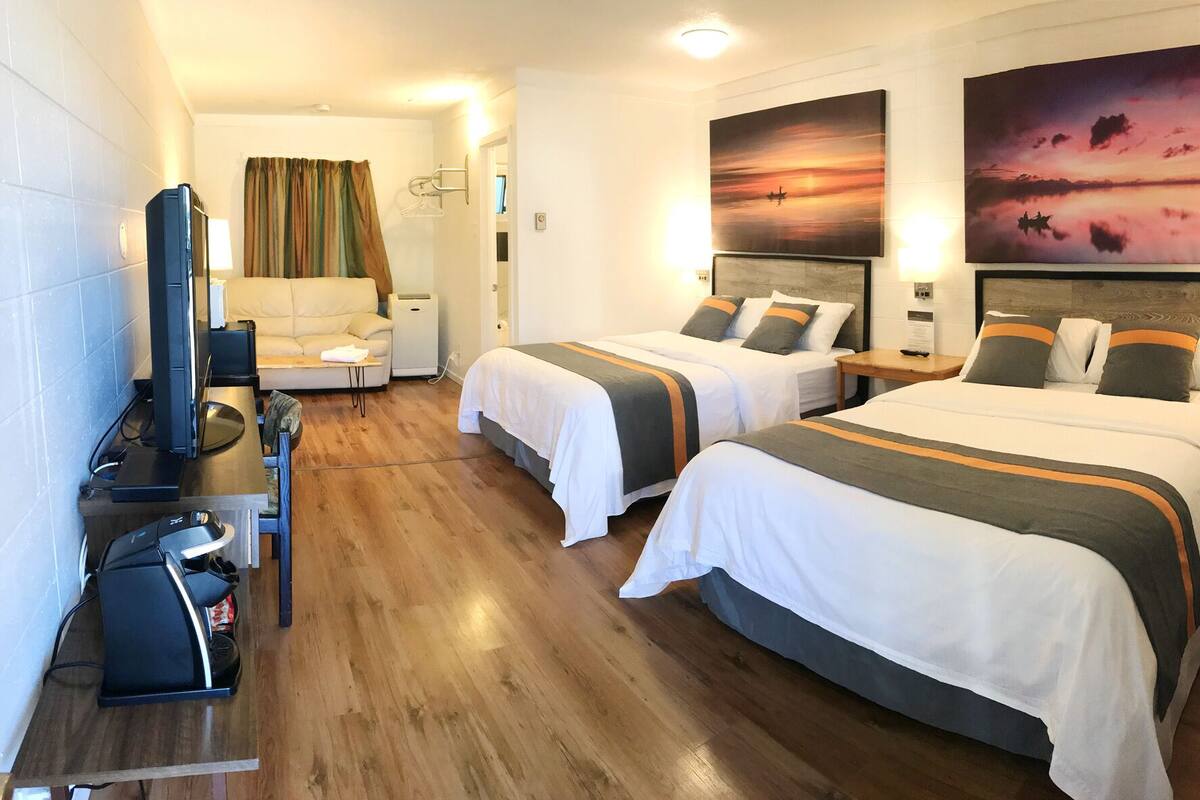 A hotel room with two beds, a desk with a computer, a TV, and artwork on the walls.