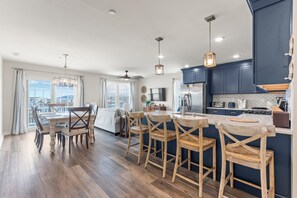 Een moderne keuken met donkerblauwe kastjes, een roestvrijstalen koelkast en een eethoek met houten stoelen en een witte tafel.