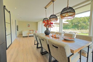 Ein moderner Essbereich mit Holztisch, beigefarbenen Polsterstühlen und einer Vase mit roten Blumen.