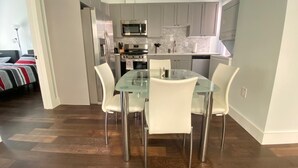 Una cocina moderna con armarios blancos, electrodomésticos de acero inoxidable y una mesa de comedor de vidrio con sillas blancas.