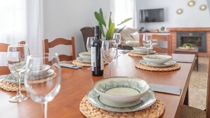 Et spisebord dækket med tallerkener, skåle og vinglas, med en vinflaske og et fjernsyn i baggrunden.