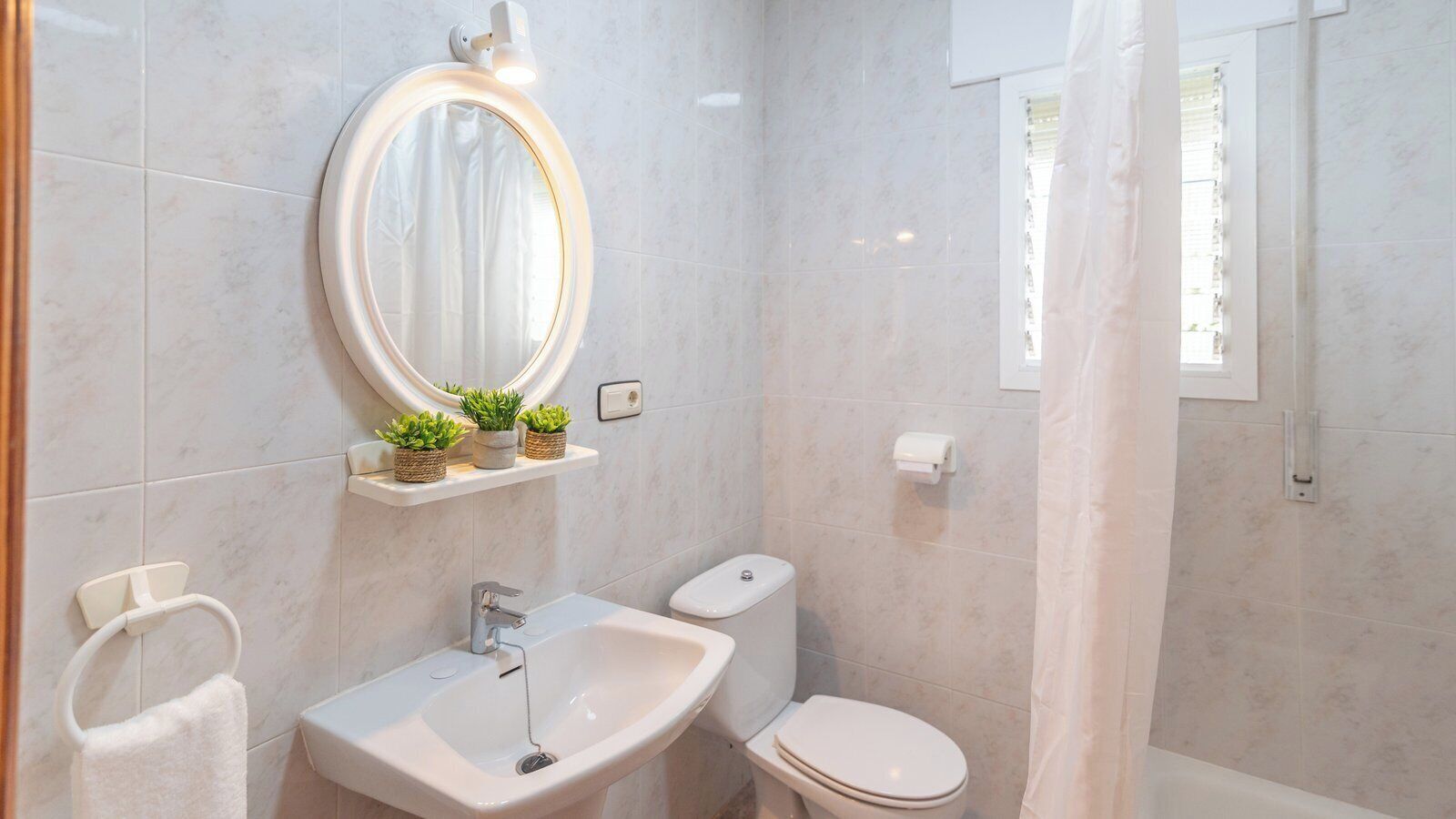 A bathroom with a white sink, a toilet, a mirror with a light, and a shower curtain.