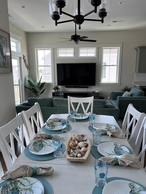 Spiseområde med et bord dækket til seks personer, et fjernsyn over bordet, og en loftsvifte.