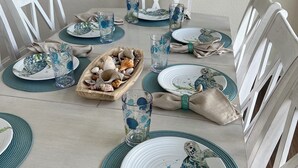 Een eettafel gedekt met borden, glazen en een decoratie van schelpen.