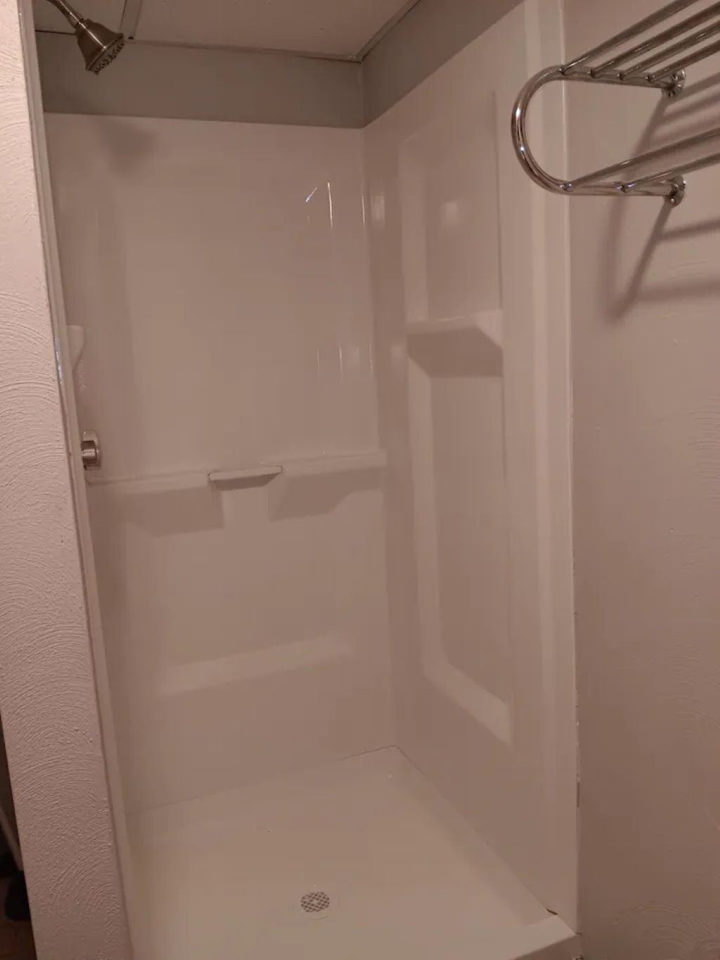 Un petit espace douche fermé, équipé d’un pommeau de douche en métal et d’un porte-serviettes en métal.