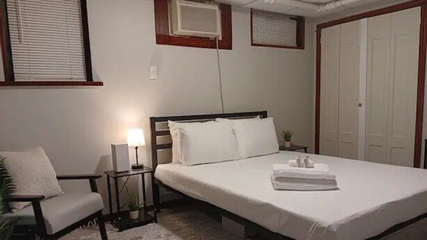 Een keurig opgemaakt slaapkamer met een bed, nachtkastje, lamp en een stoel.