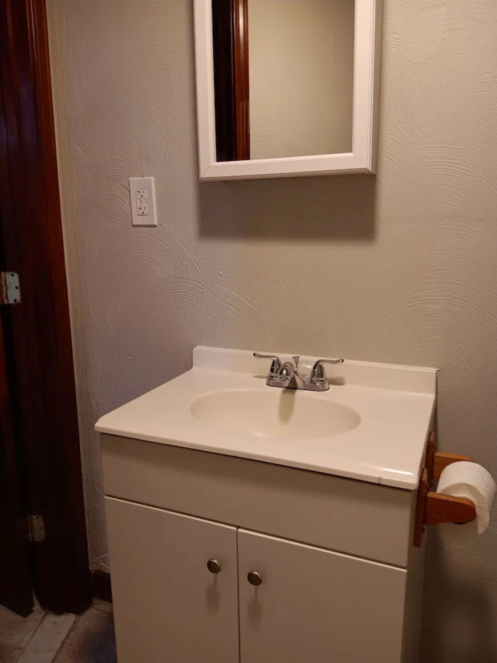 A bathroom with a white sink, a mirror above it, and a wooden door.