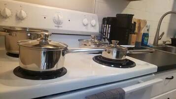 Une cuisine avec un fourneau blanc, deux casseroles sur les brûleurs, une machine à café noire et un évier avec un robinet.