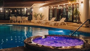 Piscina con sillas de descanso y un jacuzzi, rodeada por una zona cubierta con guirnaldas de luces.
