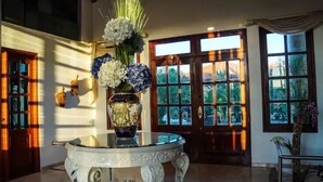 Un amplio vestíbulo con una mesa de vidrio, un jarrón decorativo con flores y vistas al exterior a través de grandes ventanales.
